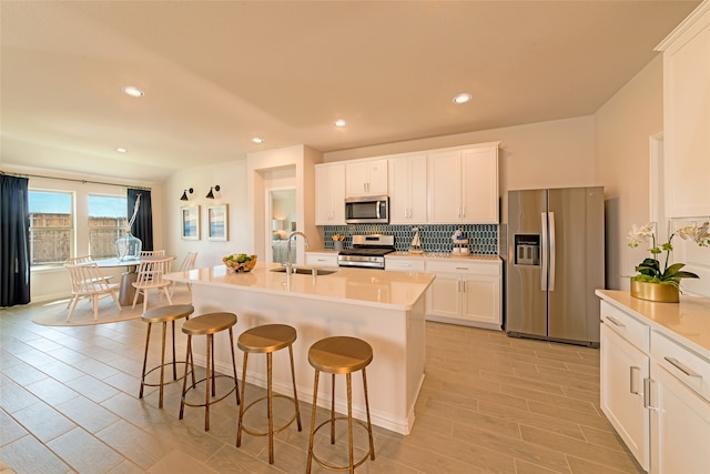 kitchen featuring a center island with sink, stainless steel appliances, white cabinetry, sink, and a breakfast bar area