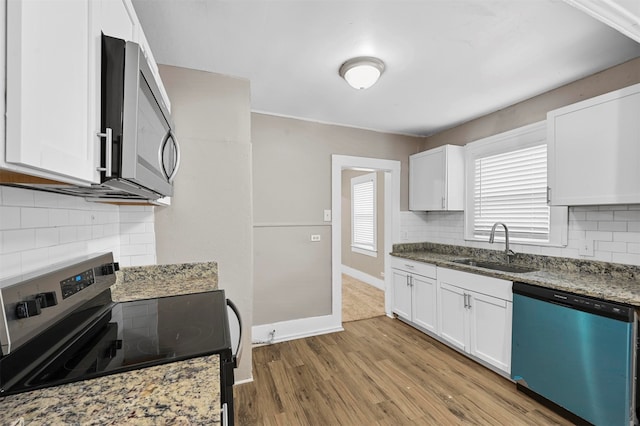 kitchen with white cabinets, appliances with stainless steel finishes, light hardwood / wood-style flooring, dark stone countertops, and sink