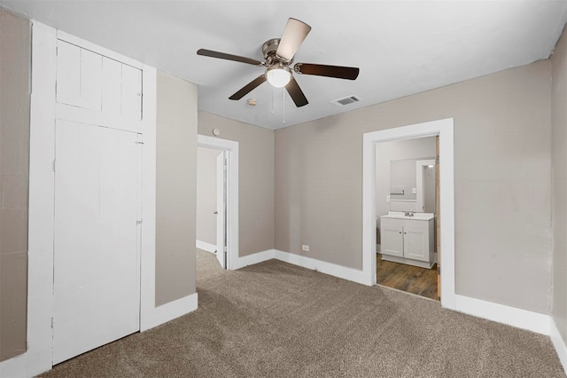 unfurnished bedroom with dark colored carpet, a closet, sink, ensuite bathroom, and ceiling fan