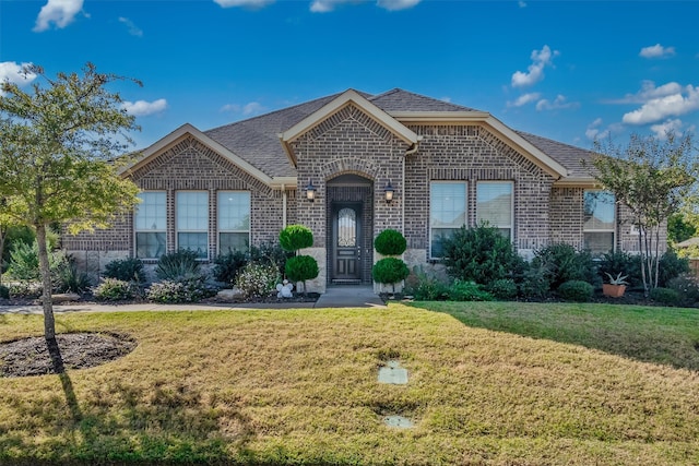 french country style house with brick siding and a front yard