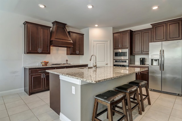 kitchen with sink, a kitchen bar, stainless steel appliances, custom exhaust hood, and a center island with sink