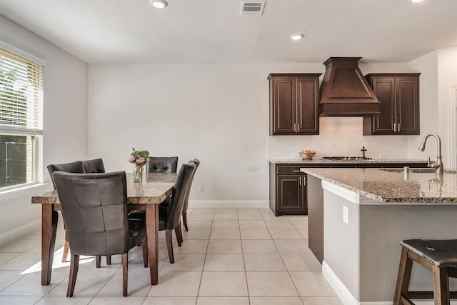 kitchen with light stone counters, dark brown cabinets, sink, and custom exhaust hood