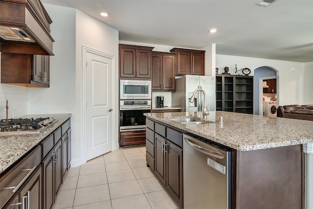 kitchen featuring light tile patterned floors, appliances with stainless steel finishes, premium range hood, a kitchen island with sink, and sink