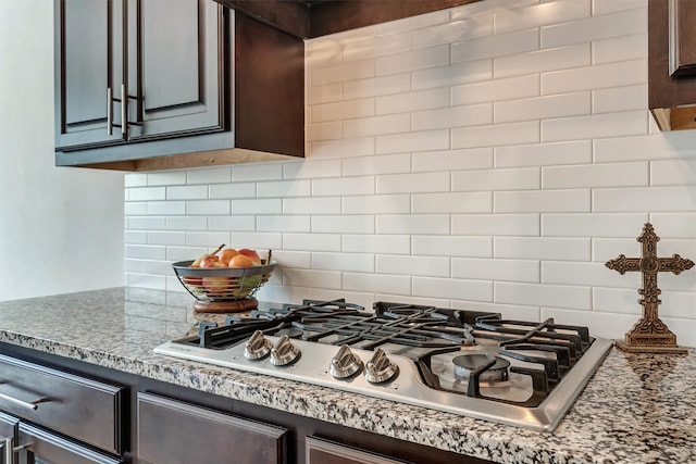 kitchen with dark brown cabinetry, stainless steel gas stovetop, decorative backsplash, and light stone counters