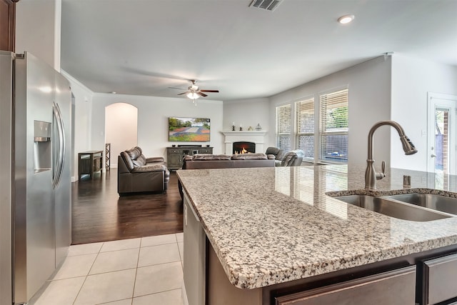 kitchen with a center island with sink, stainless steel fridge with ice dispenser, light stone countertops, light hardwood / wood-style flooring, and sink