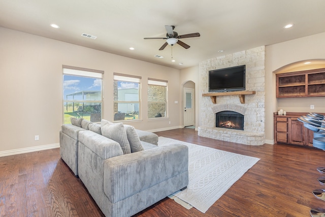 living room featuring a stone fireplace, ceiling fan, and dark hardwood / wood-style flooring