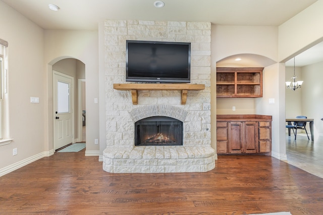 unfurnished living room featuring a notable chandelier, a stone fireplace, and dark hardwood / wood-style flooring