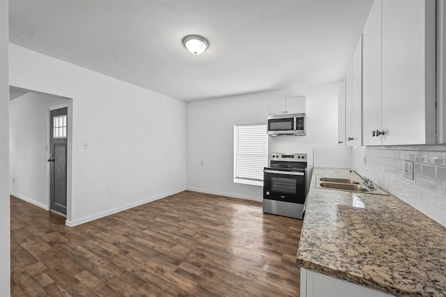 kitchen featuring white cabinets, appliances with stainless steel finishes, light stone countertops, dark wood-type flooring, and sink