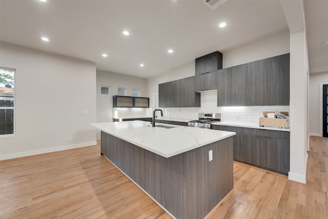 kitchen with tasteful backsplash, an island with sink, light hardwood / wood-style flooring, stainless steel range with gas cooktop, and sink