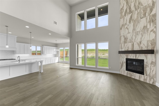 unfurnished living room featuring sink, a fireplace, a high ceiling, dark wood-type flooring, and an inviting chandelier