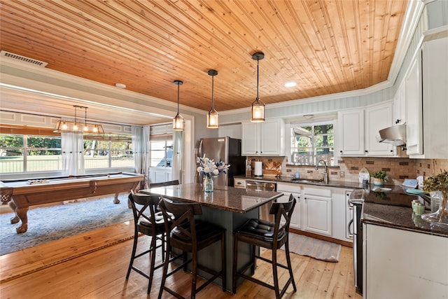 kitchen featuring a kitchen island, stainless steel appliances, dark stone countertops, light wood-type flooring, and white cabinetry