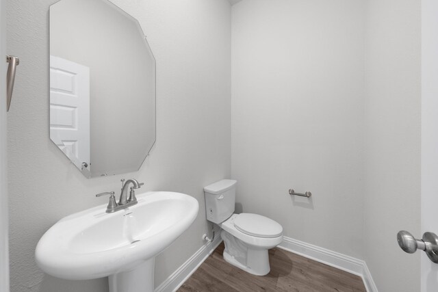 half bath featuring toilet, wood finished floors, baseboards, and a sink