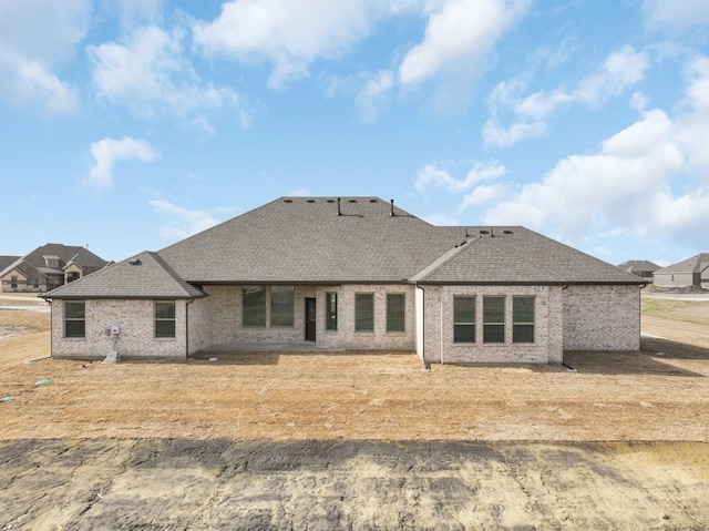 back of property featuring brick siding and roof with shingles