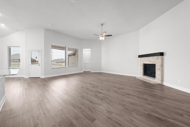 unfurnished living room with a fireplace with raised hearth, baseboards, ceiling fan, lofted ceiling, and wood finished floors