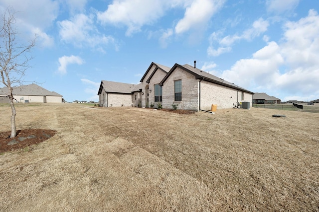 rear view of house featuring stone siding, cooling unit, and fence