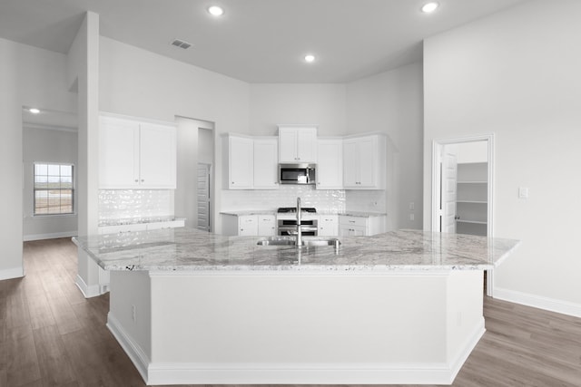 kitchen with a spacious island, stainless steel microwave, visible vents, white cabinetry, and a sink