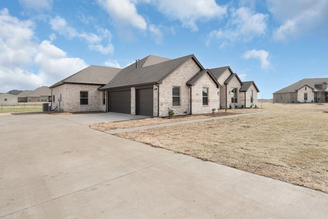 french country style house with driveway, cooling unit, roof with shingles, an attached garage, and brick siding