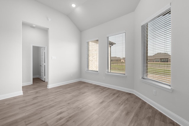 spare room with vaulted ceiling, light wood-style flooring, and baseboards