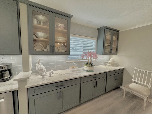 bar featuring decorative backsplash, light stone countertops, light wood-type flooring, ornamental molding, and gray cabinetry