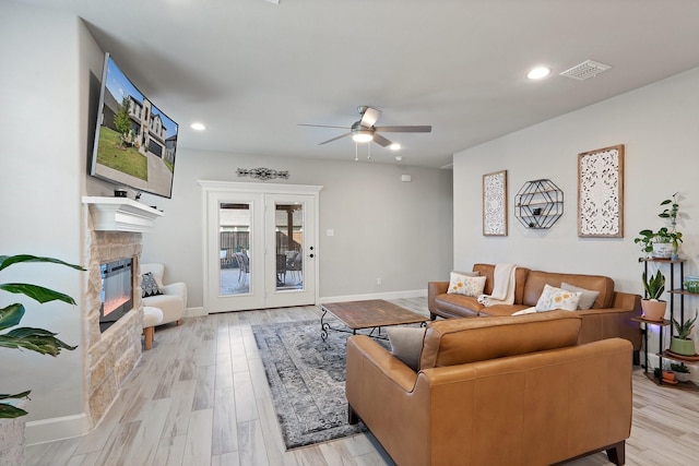 living room with ceiling fan, a stone fireplace, and light wood-type flooring