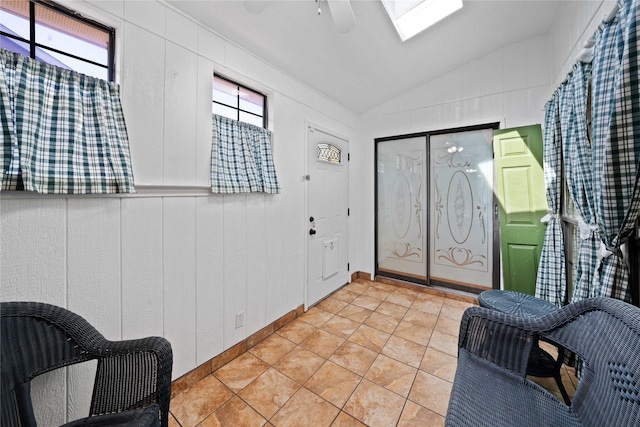 entryway with ceiling fan, light tile patterned flooring, and vaulted ceiling with skylight