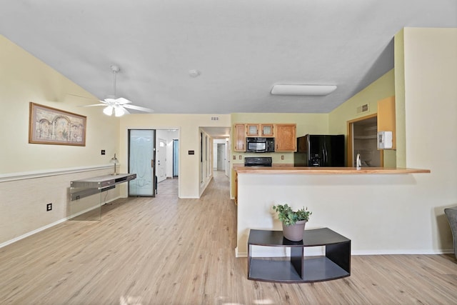 kitchen with kitchen peninsula, vaulted ceiling, black appliances, and light hardwood / wood-style flooring