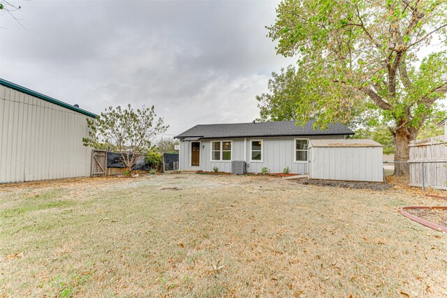 rear view of house with central air condition unit, a storage shed, and a lawn