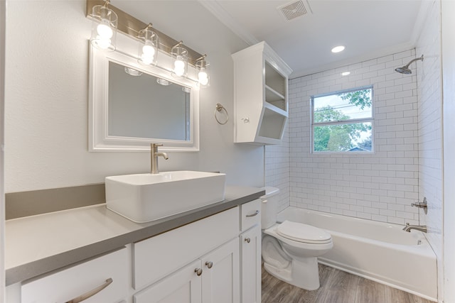 full bathroom featuring toilet, wood-type flooring, ornamental molding, tiled shower / bath combo, and vanity