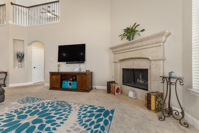 carpeted living room with a high end fireplace and a high ceiling