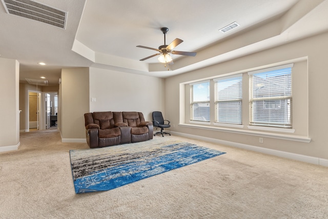 living room with ceiling fan, a tray ceiling, and carpet flooring