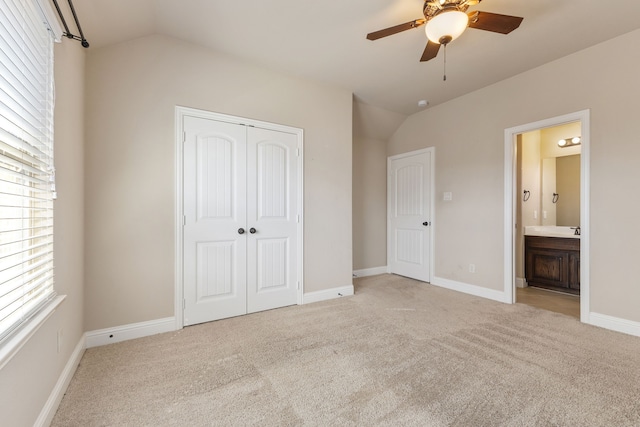 unfurnished bedroom featuring a closet, ensuite bath, vaulted ceiling, light colored carpet, and ceiling fan