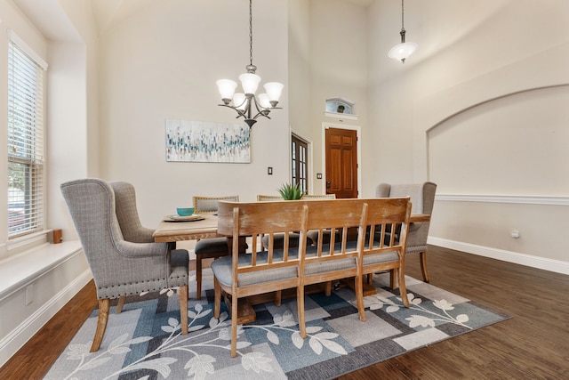 dining area featuring a high ceiling, a notable chandelier, a healthy amount of sunlight, and dark hardwood / wood-style flooring