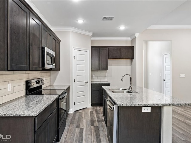 kitchen featuring dark wood-type flooring, a center island with sink, sink, crown molding, and appliances with stainless steel finishes