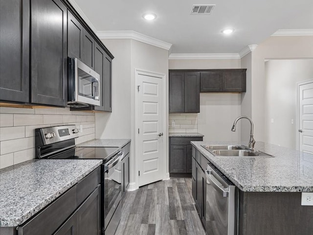 kitchen featuring dark wood-type flooring, an island with sink, stainless steel appliances, ornamental molding, and sink