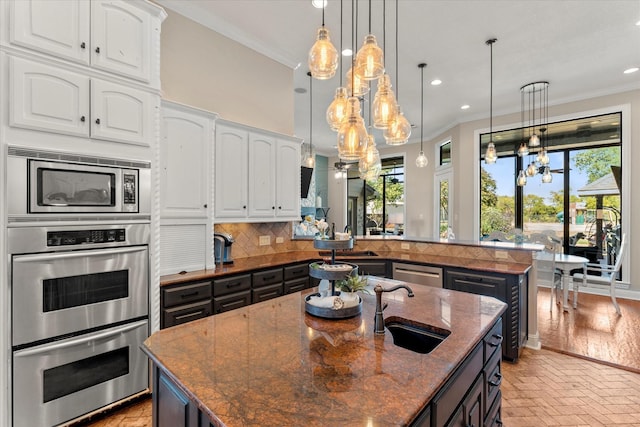 kitchen with white cabinetry, tasteful backsplash, dark stone countertops, decorative light fixtures, and a kitchen island with sink