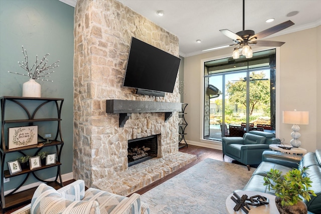 living room with wood-type flooring, a stone fireplace, ceiling fan, and ornamental molding