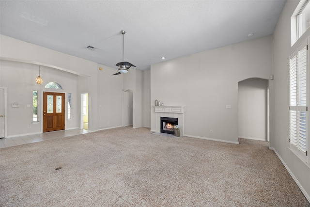 unfurnished living room with ceiling fan, a textured ceiling, a tile fireplace, a high ceiling, and light colored carpet