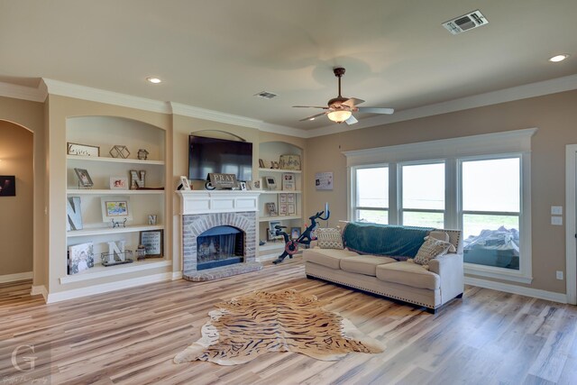 living room with dark wood-type flooring, ornamental molding, a brick fireplace, and built in shelves