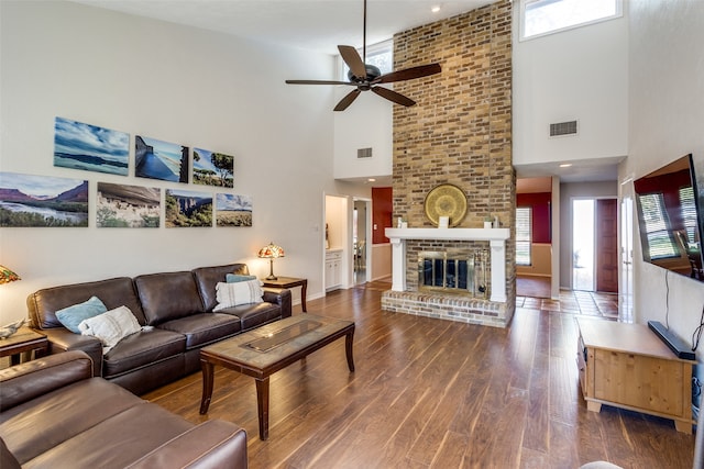 living room featuring hardwood / wood-style floors, a fireplace, a towering ceiling, and ceiling fan