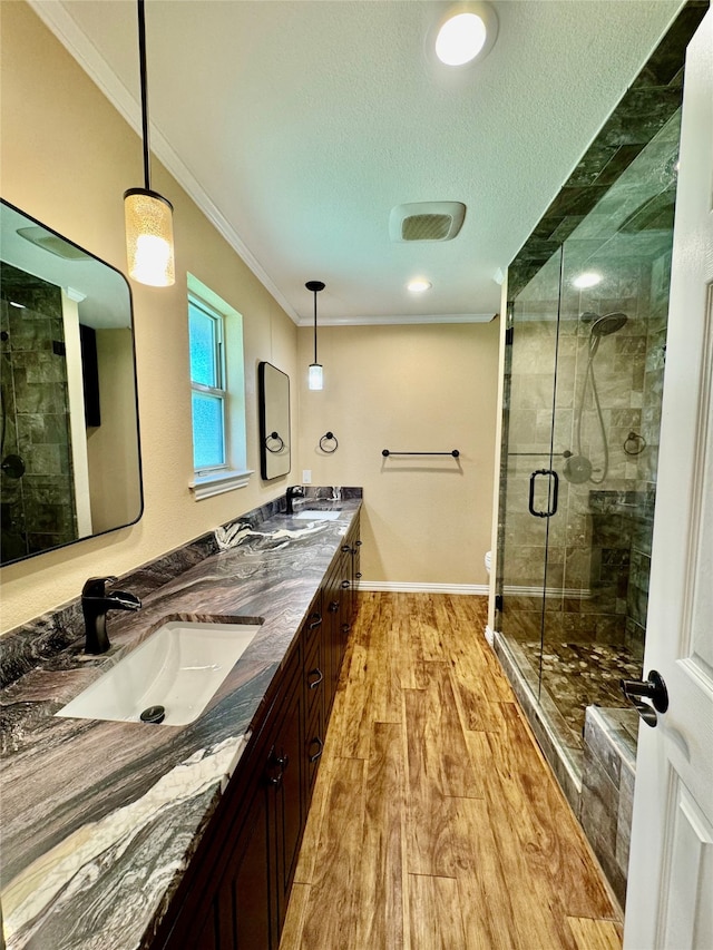 bathroom with wood-type flooring, ornamental molding, vanity, a shower with door, and a textured ceiling