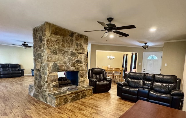 living room featuring a stone fireplace, crown molding, hardwood / wood-style floors, and ceiling fan with notable chandelier