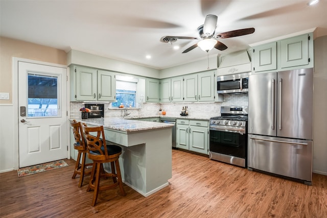 kitchen with a breakfast bar, light stone counters, appliances with stainless steel finishes, and light hardwood / wood-style flooring