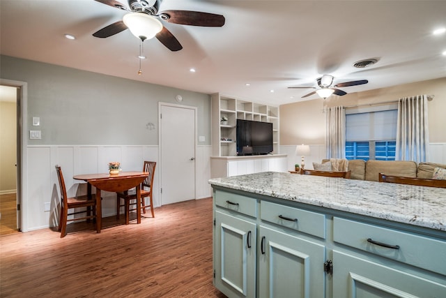 kitchen with built in shelves, ceiling fan, light stone countertops, and dark wood-type flooring