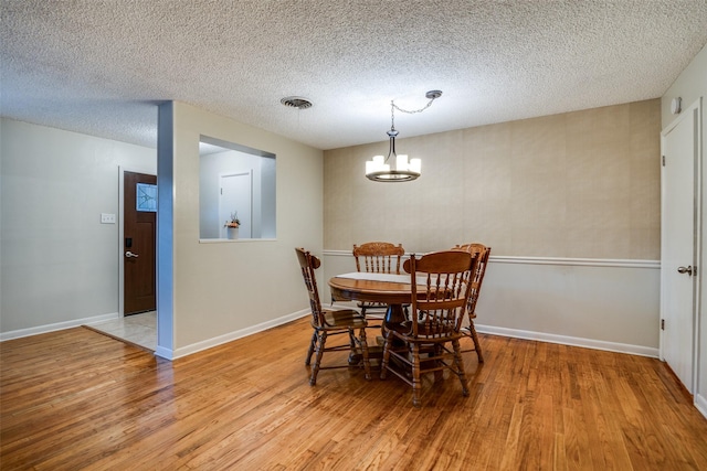 dining space with light hardwood / wood-style flooring, a textured ceiling, and an inviting chandelier