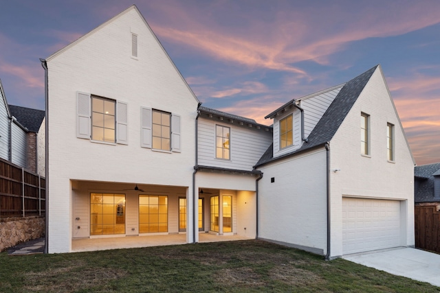 back house at dusk with a patio area, a yard, and a garage