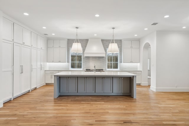 kitchen with white cabinets, premium range hood, a kitchen island with sink, and hanging light fixtures