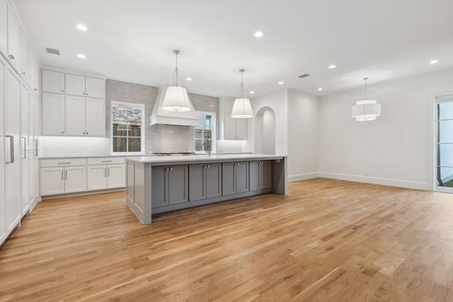 kitchen with custom exhaust hood, a spacious island, pendant lighting, light hardwood / wood-style floors, and white cabinetry