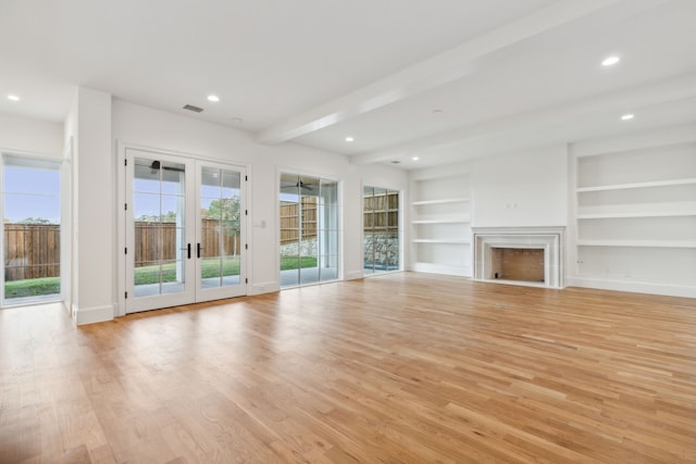 unfurnished living room with beam ceiling, built in features, light hardwood / wood-style flooring, and french doors