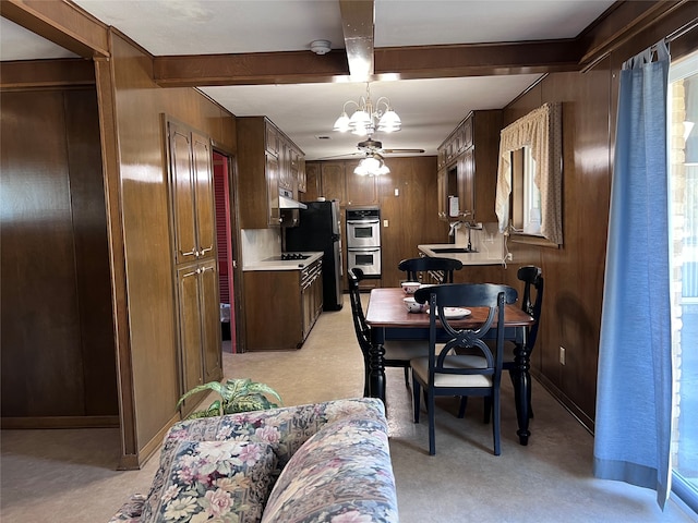 dining area featuring beamed ceiling, wooden walls, sink, and ceiling fan with notable chandelier