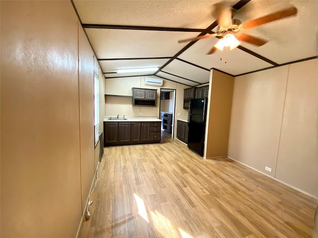 kitchen featuring sink, black fridge, vaulted ceiling, an AC wall unit, and light wood-type flooring